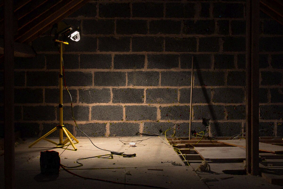 Dimly lit residential attic space under renovation with a work lamp