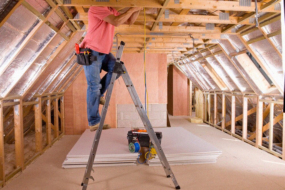 Electrician working on wiring from a ladder inside an attic space