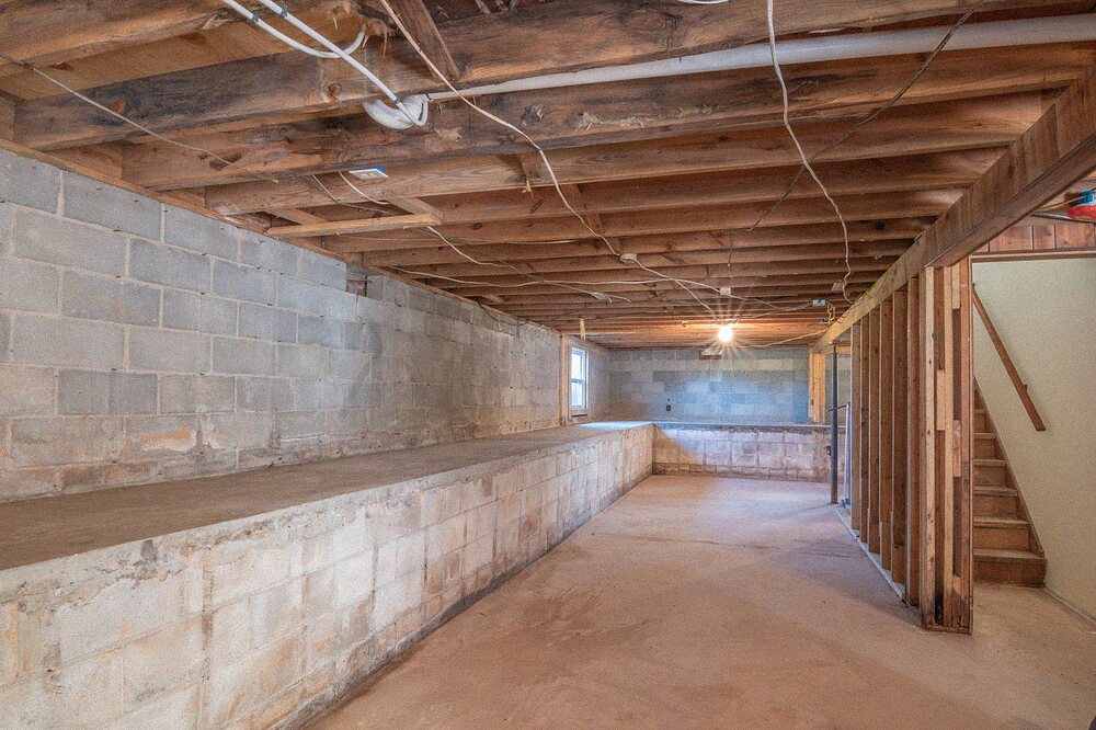 Empty under-floor space with exposed timber beams and concrete walls
