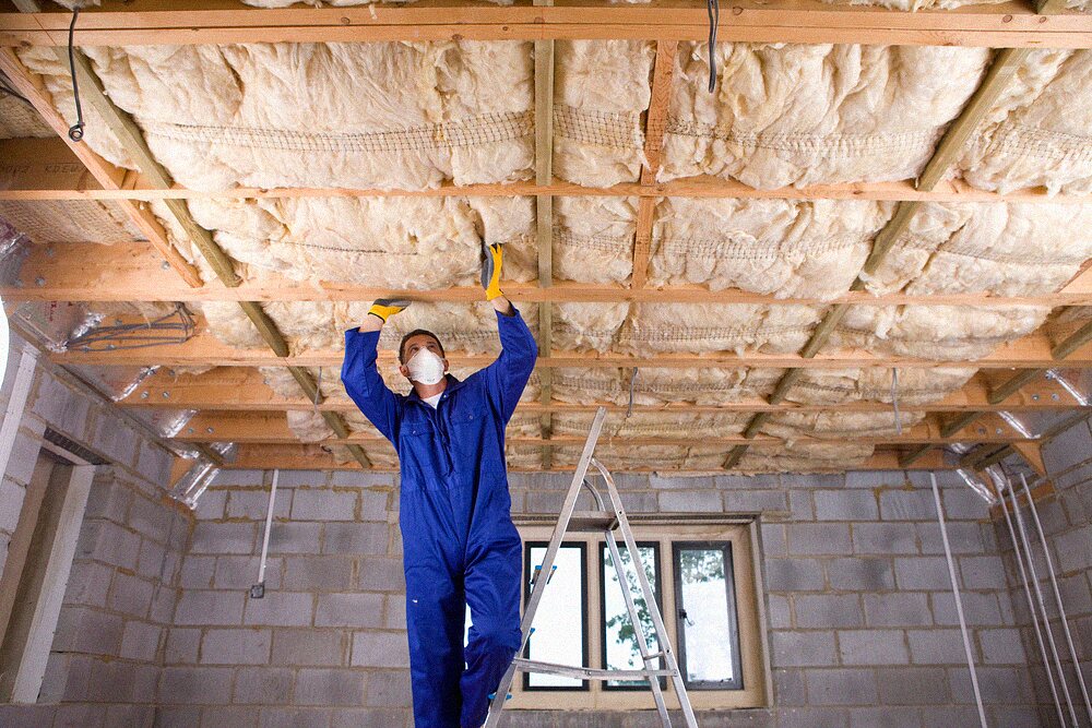 Worker in coveralls and a protective mask on a ladder inside an attic
