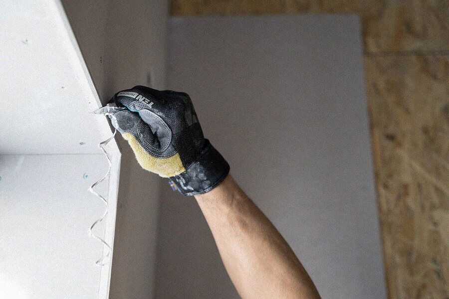 Gloved hand applying filler to a repaired section of interior wall